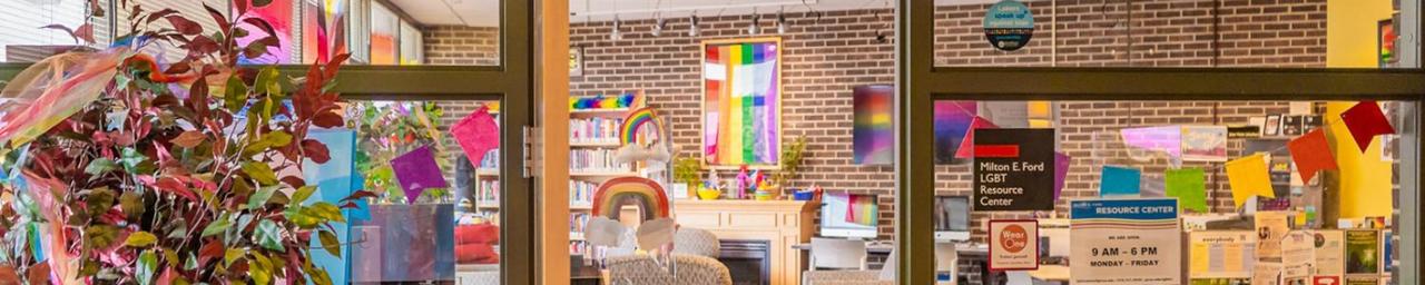 Looking through the door and glass windows of the LGBT Resource Center. It is bright and colorful inside, with a visible rainbow flag. Photo credit: Macayla with Lanthorn 2022